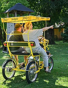 Two people are sitting in a pedal car and driving through the garden of the Pechtlgut in Lofer