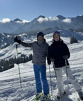 Zwei Skifahrer auf einer Skipiste mit beschneite Berge im Hintergrund