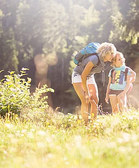 A mother and her child in front of a forest on a sunny summer day